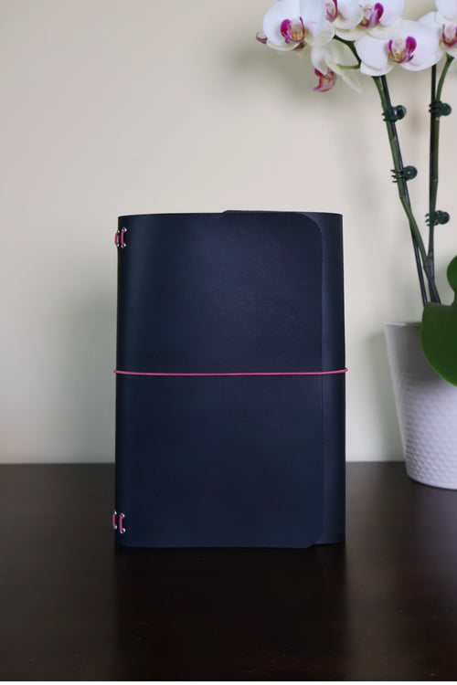 Dark blue cylindrical device with pink accents on a wooden surface, next to a white vase with flowers.