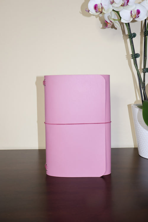 Pink cylindrical container on a wooden surface with a beige wall and white orchids in the background.