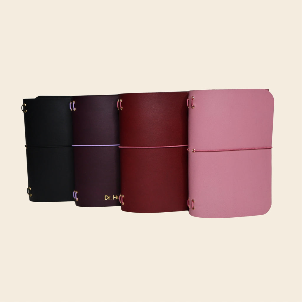 Four notebooks in black, purple, red, and pink on a beige background