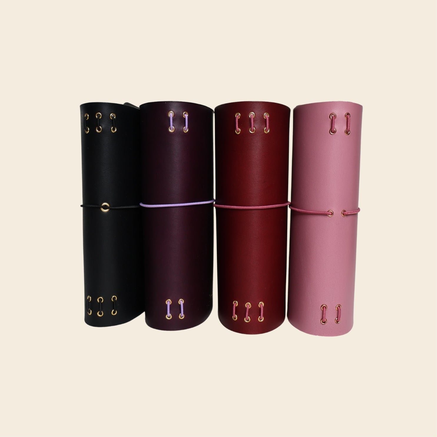 Four leather journals in black, violet, red, and mauve on a beige background