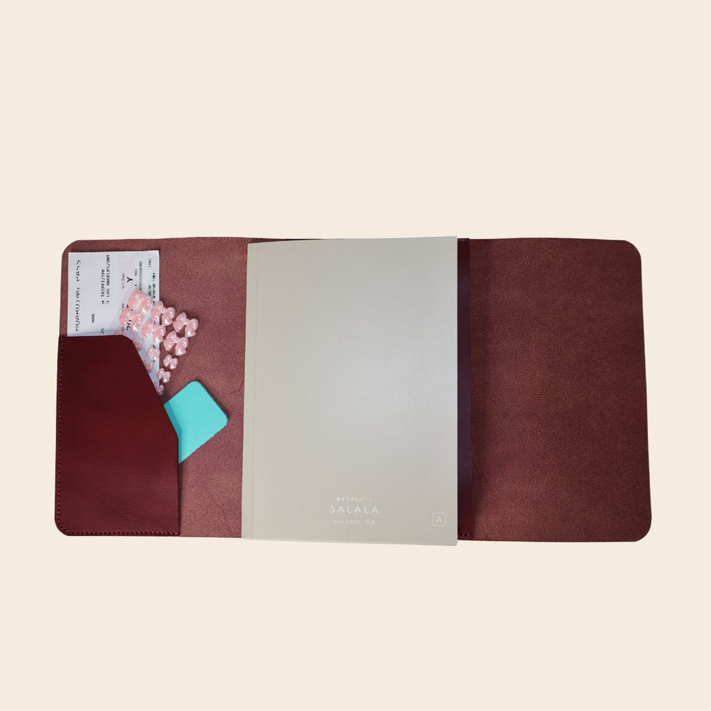 Brown leather journal with a card and pink stickers on a beige background