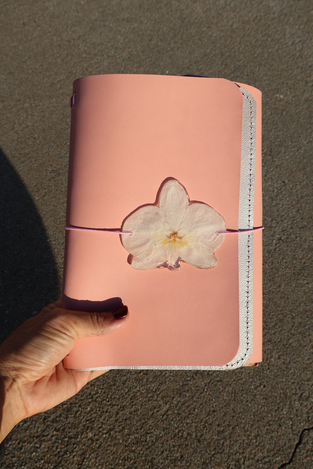 Pink notebook with a white flower attached, held by a hand on a brown surface