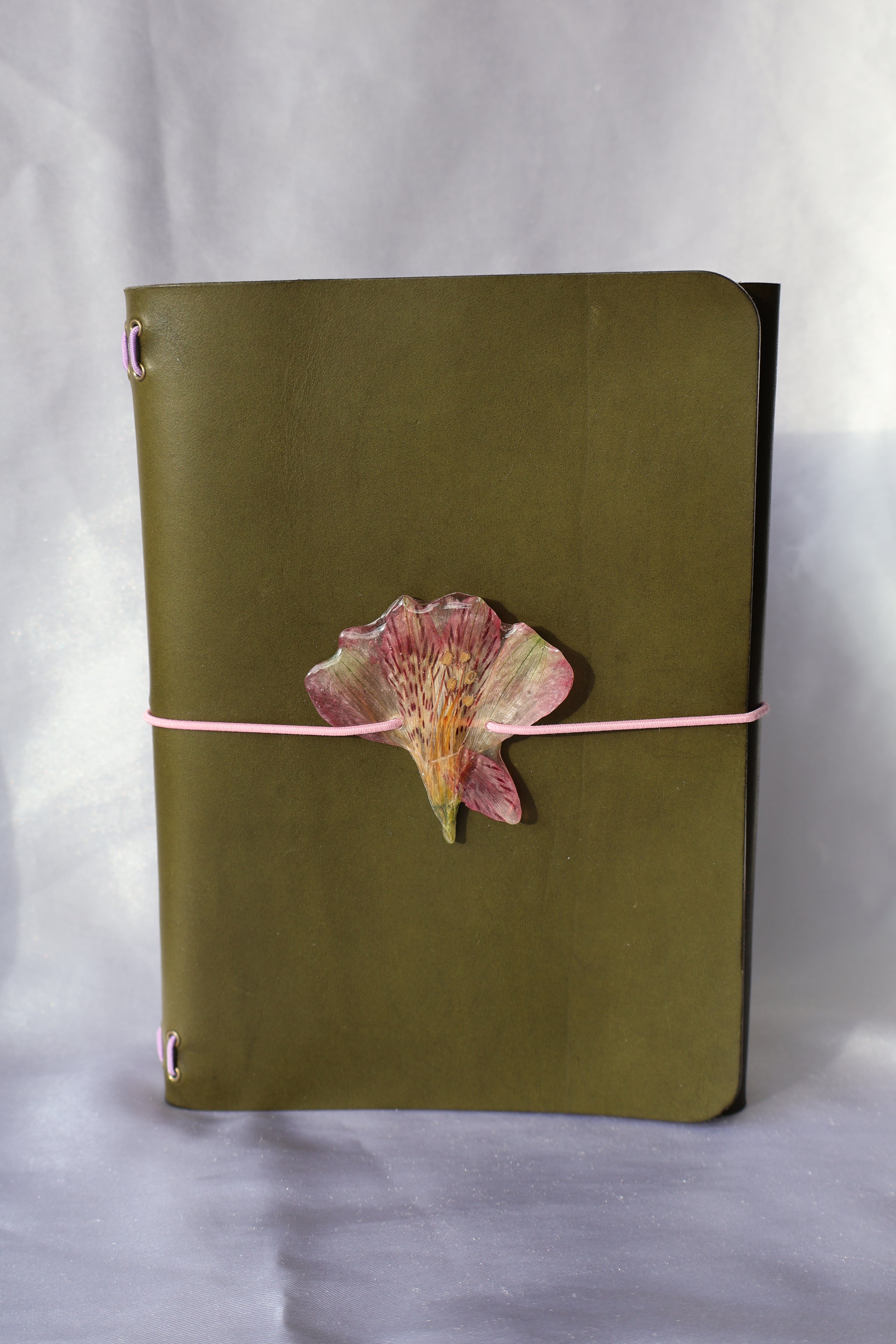 Green journal with a pink ribbon and Peru lily on a white background