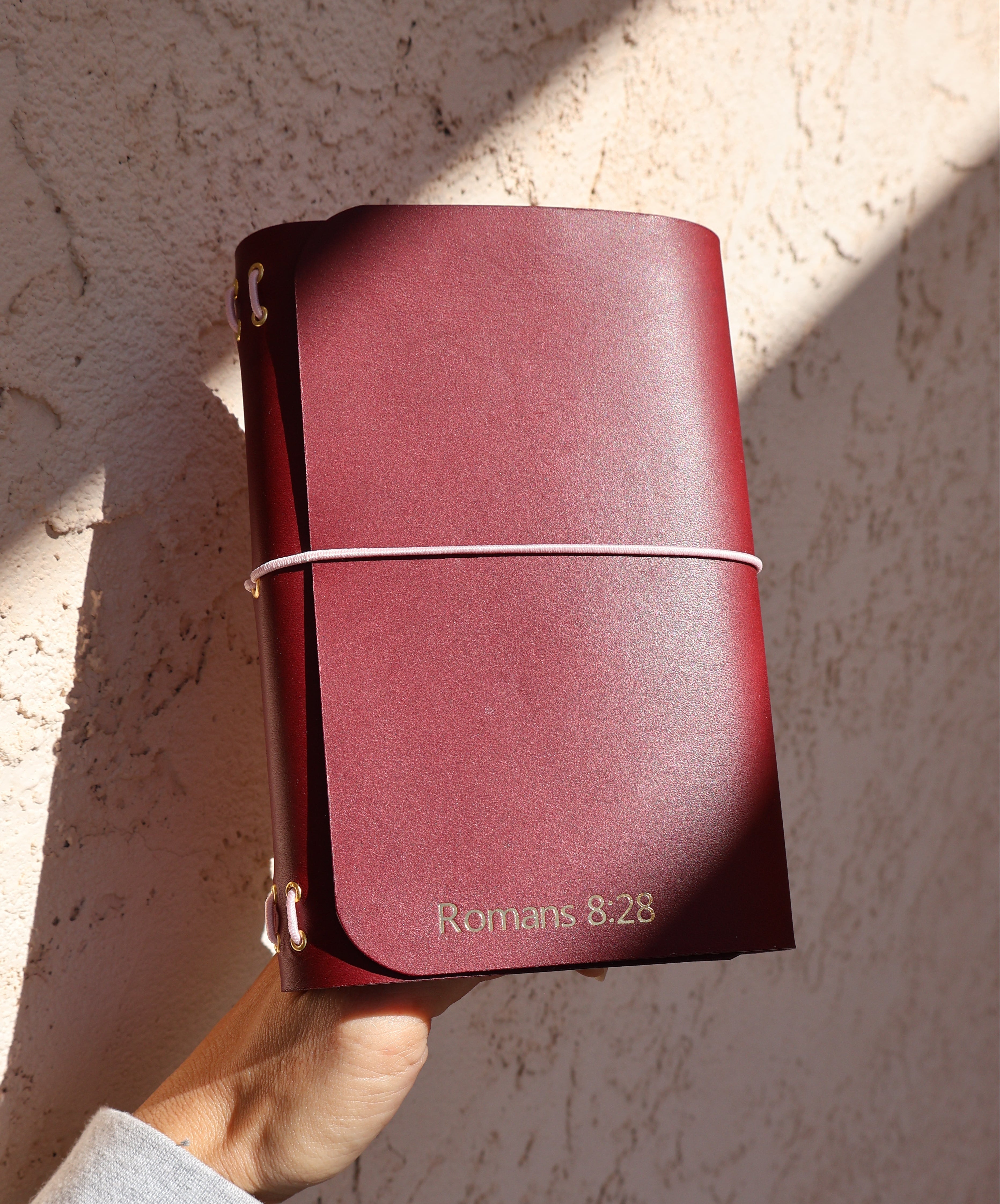Hand holding a maroon leather-bound book with 'Rogers & SONS' embossed on it against a textured beige background.