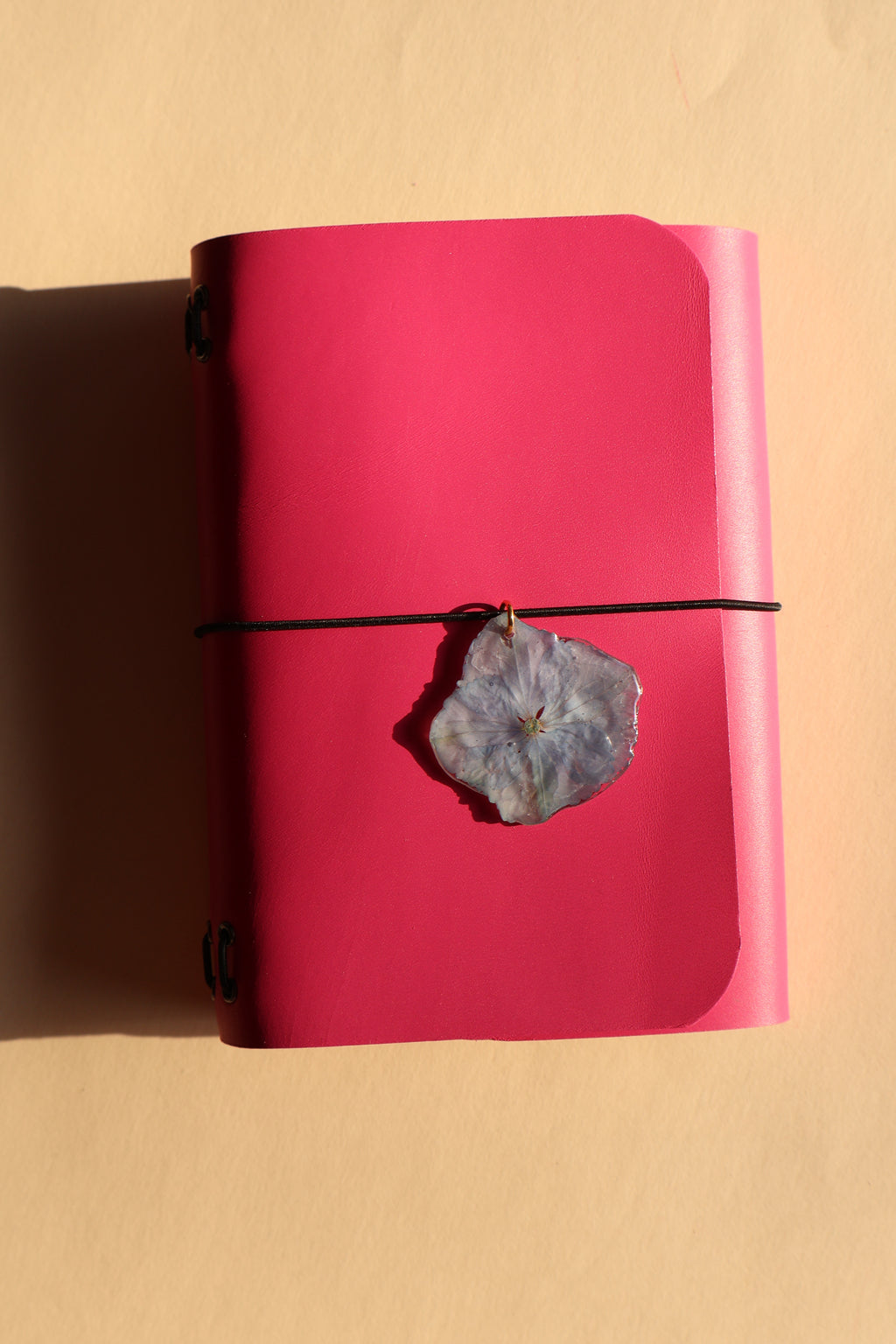 Pink notebook with a stone pendant on a beige background