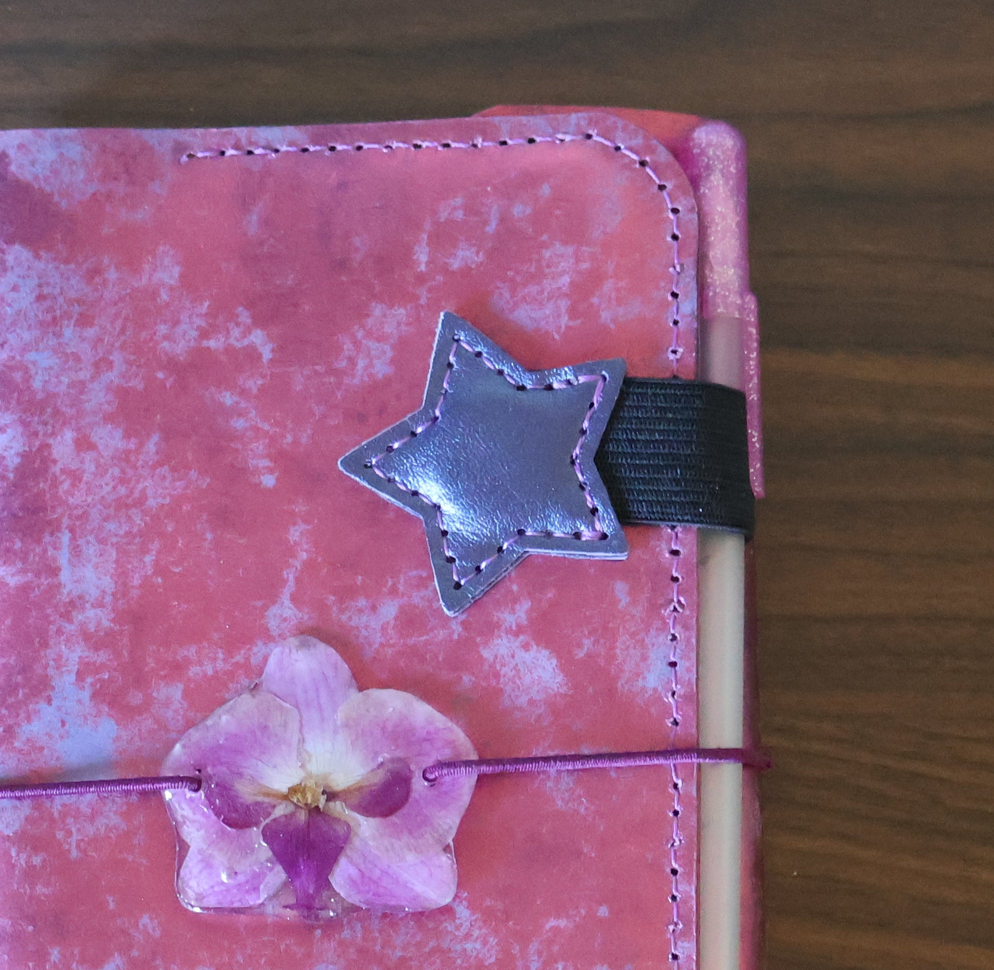 Pink floral-patterned phone case with a star and flower design on a wooden surface