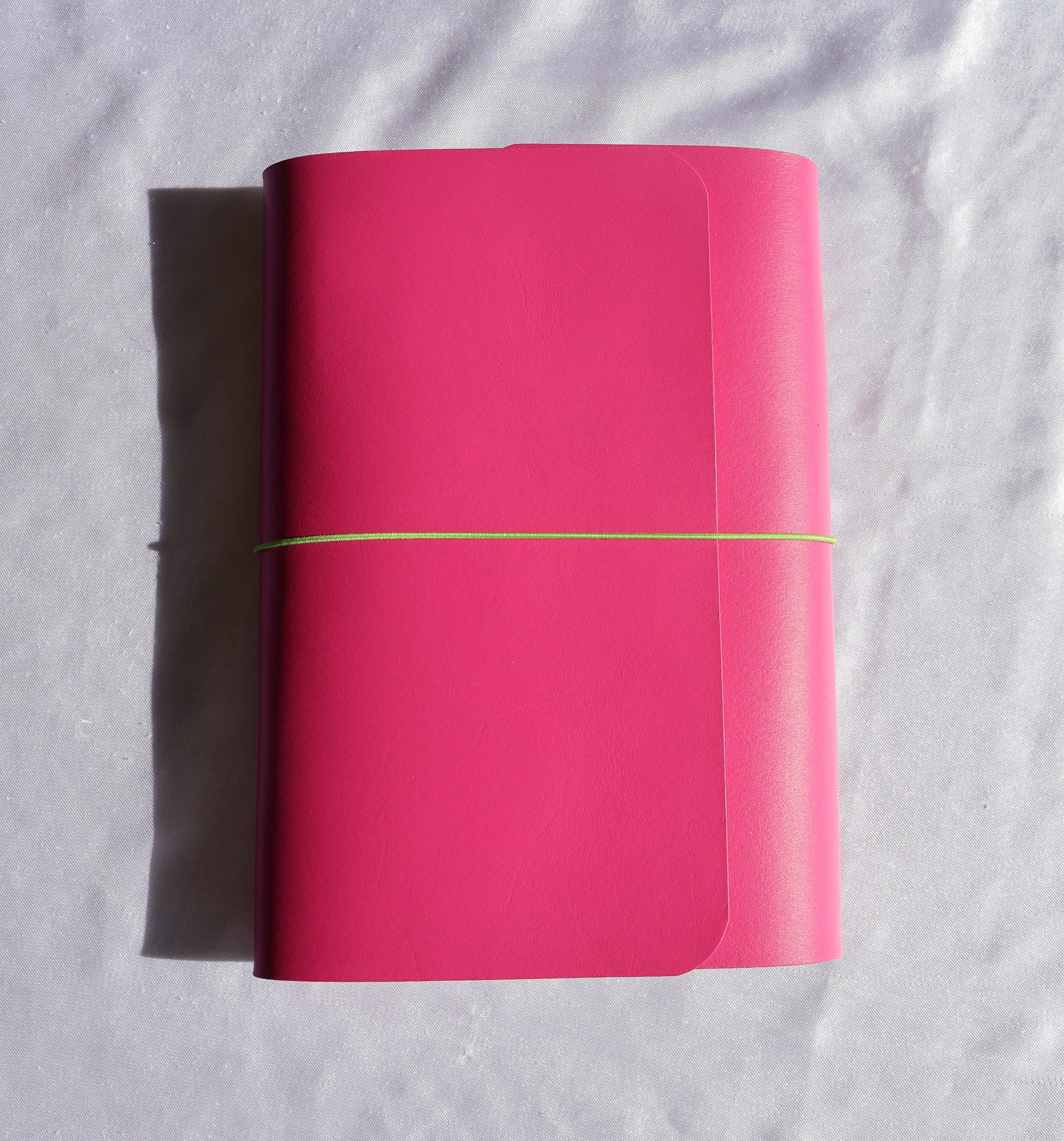Pink notebook with a yellow elastic band on a white fabric background