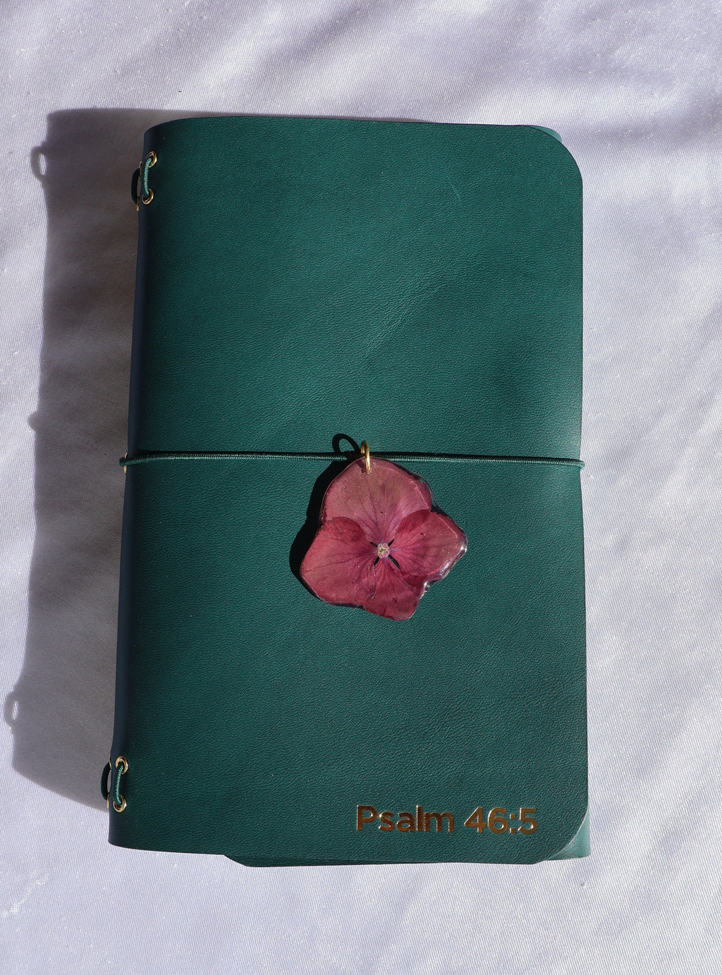 Green leather wallet with a pink flower on a white fabric background