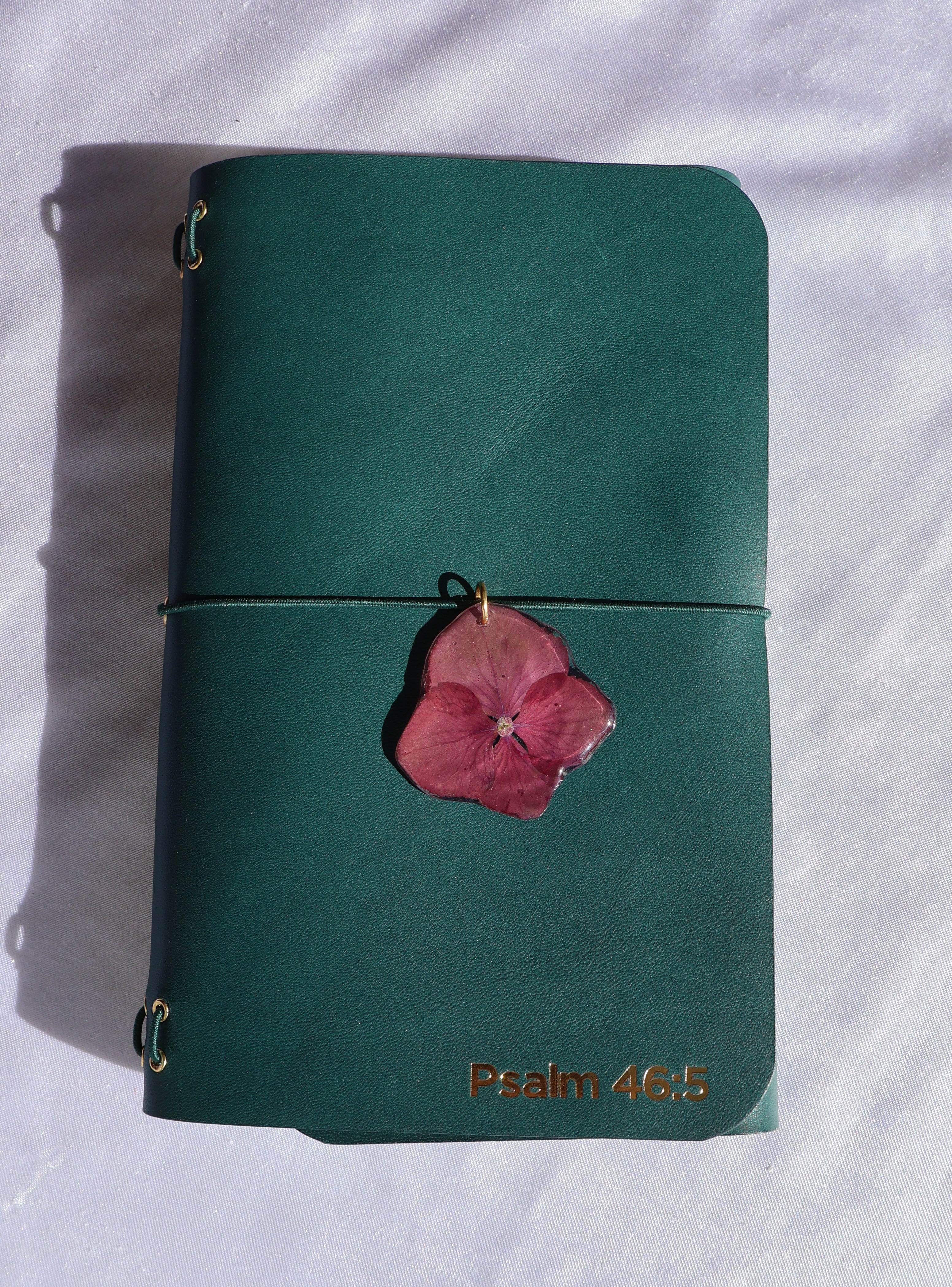 Green leather wallet with a pink flower on a white fabric background
