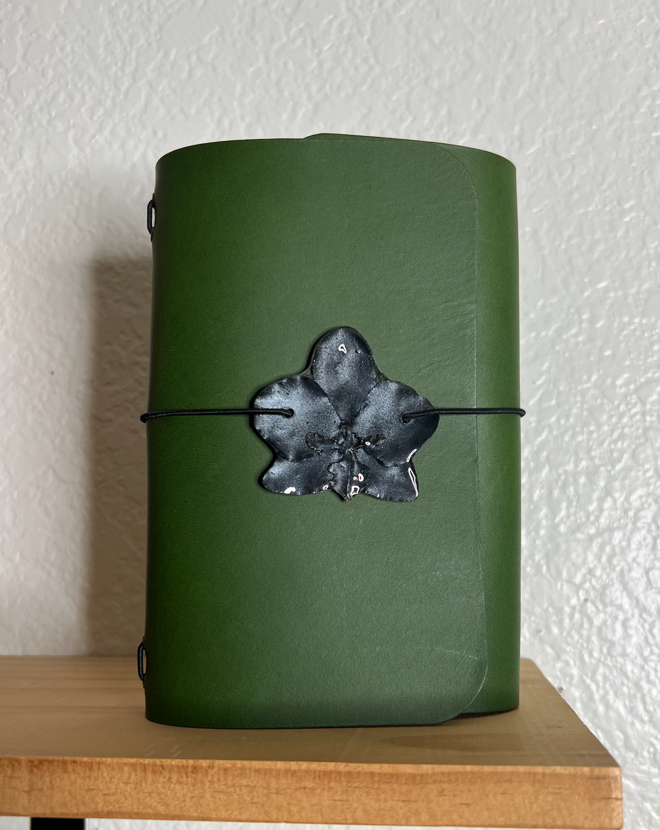 small black flower charm on a green journal on a shelf