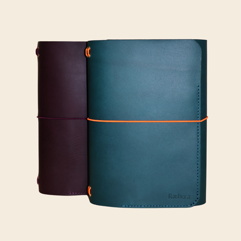 Two leather-bound notebooks, one purple and one blue, on a beige background.