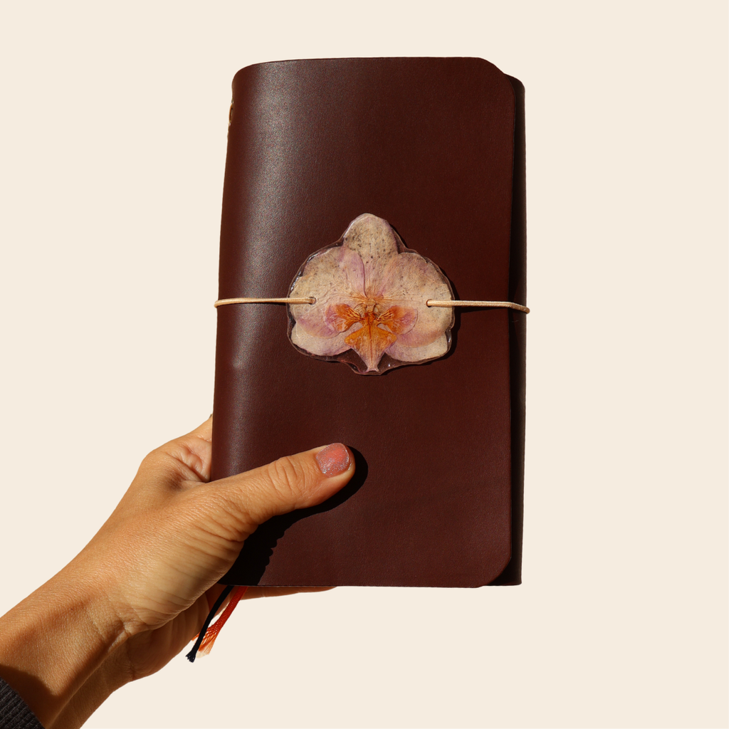 Brown leather notebook with a pressed flower design held by a hand on a beige background
