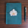Teal notebook with a white flower decoration on a wooden surface