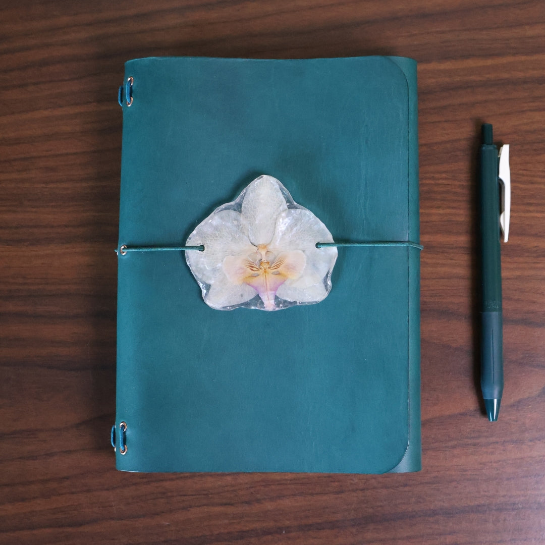 Teal notebook with a white flower decoration on a wooden surface