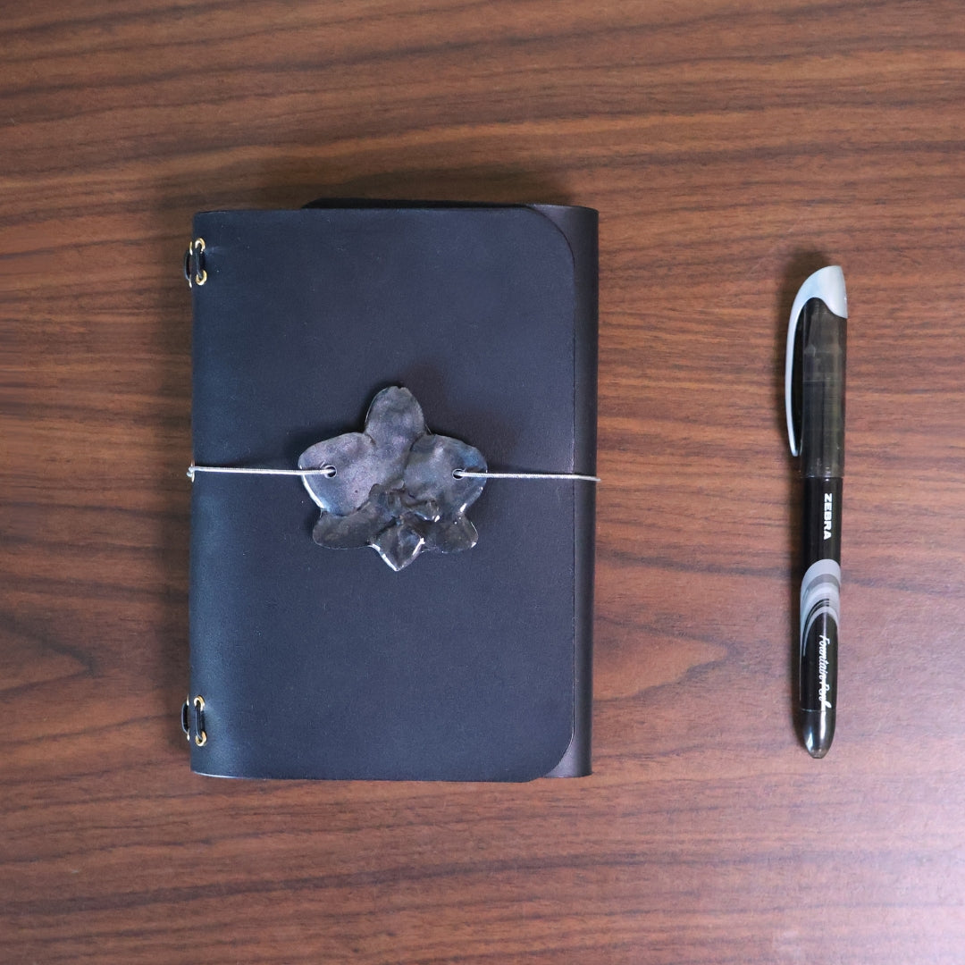 Black leather notebook with a decorative stone and pen on a wooden surface