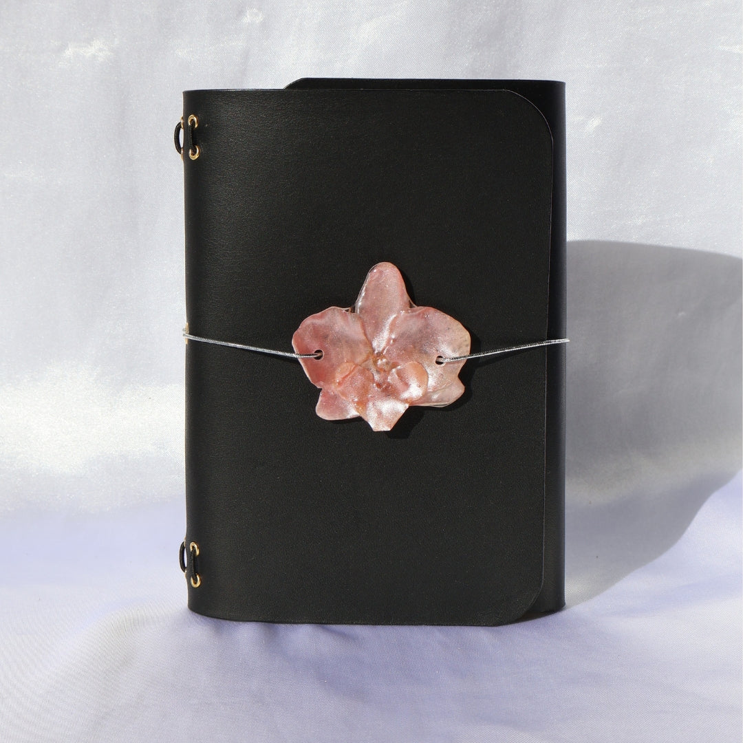 Black leather notebook with a pink flower charm on a light gray background